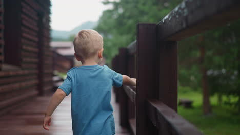 Curious-little-boy-touches-wet-wooden-railing-on-deck
