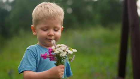 Happy-little-boy-holds-bouquet-of-wildflowers-in-park