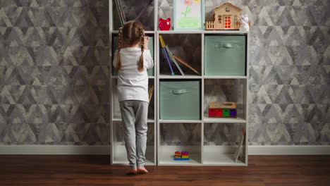Funny-girl-walks-to-take-toys-out-of-box-on-rack-at-home