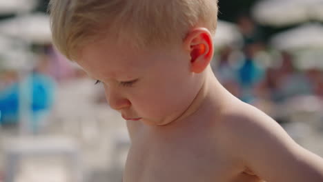 Pensive-little-child-stands-on-public-beach-at-marine-resort