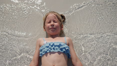 Little-girl-in-swimsuit-waves-hands-in-surfline-on-beach