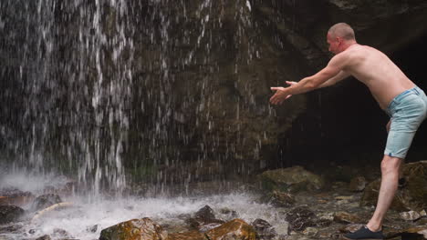 Man-hiker-catches-falling-down-water-drops-near-old-rock