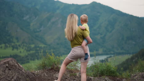 Mother-holds-toddler-and-points-to-river-in-mountain-valley
