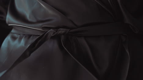 Woman-unties-belt-of-elegant-leather-coat-on-dark-background
