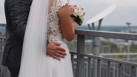 Man-groom-embraces-beloved-woman-in-wedding-dress-on-bridge