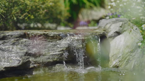 Tiny-waterfall-with-large-stone-and-pond-in-summer-park