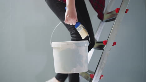 Woman-goes-up-step-ladder-holding-paint-brush-and-bucket