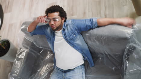 Afro-American-man-falls-down-on-sofa-covered-with-plastic