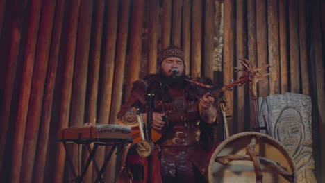Bearded-Asian-singer-in-old-clothes-plays-tovshuur-in-cabin