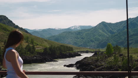 Woman-walks-along-bridge-over-wild-river-in-mountain-valley