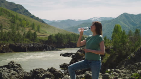 Tired-woman-drinks-water-and-looks-around-on-river-bank