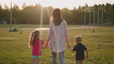Woman-with-little-son-and-daughter-walk-along-park-meadow