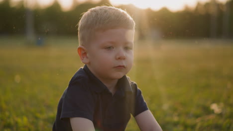 Upset-little-boy-in-black-clothes-sits-on-lawn-at-sunset