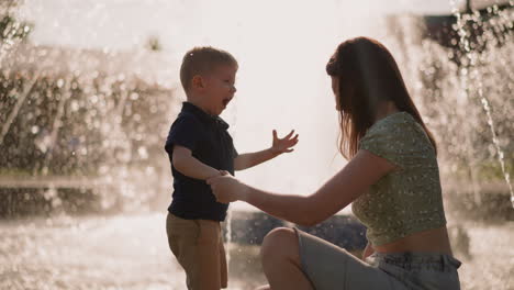 Excited-little-boy-plays-with-happy-mother-near-fountain