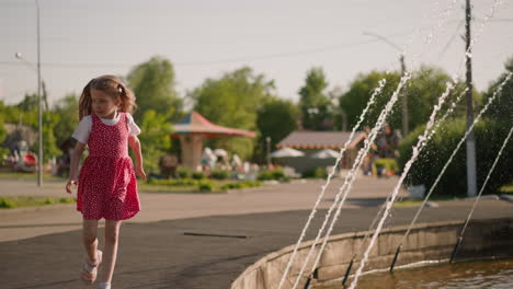 Little-girl-runs-past-fountain-with-water-jets-in-park
