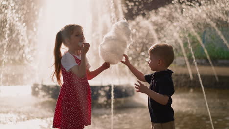 Little-girl-with-brother-eats-cotton-candy-near-fountain