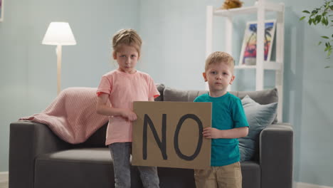 Unhappy-children-show-placard-with-word-NO-in-living-room