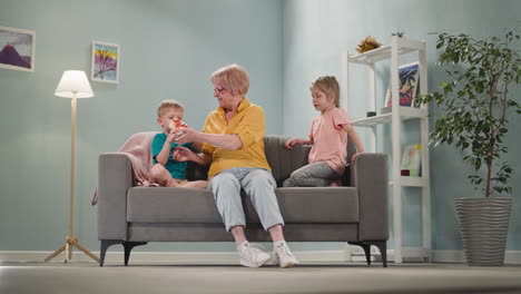 Boy-looks-at-piggy-bank-with-granny-and-elder-sister-on-sofa