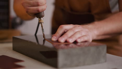 Master-processes-leather-piece-edge-with-tool-at-workplace