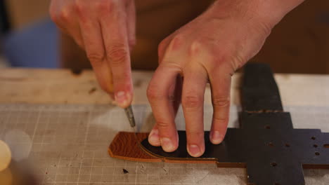 Worker-cuts-leather-belt-edge-with-knife-on-workbench