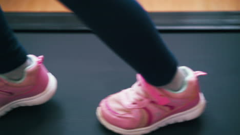 Verspielte-Mädchen-Rosa-Sneaker-Springen-Zu-Hause-Auf-Ein-Modernes-Laufband
