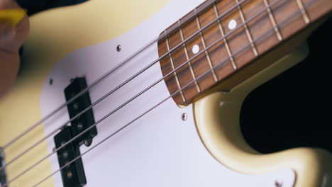 guitarist-plays-white-bass-guitar-with-yellow-pick-closeup
