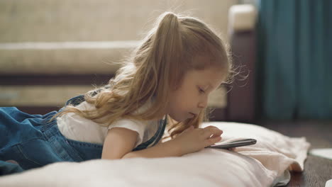 little-girl-in-denim-dress-plays-with-mobile-phone-on-floor