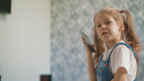 Kleines-Mädchen-Mit-Pferdeschwänzen-Spricht-Auf-Dem-Smartphone-Im-Hellen-Raum