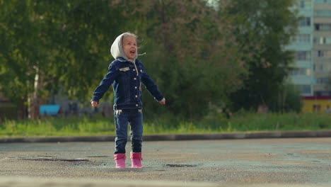 joyful-girl-in-pink-rubber-boots-and-denim-jumps-in-puddle