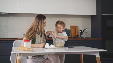 mother-teaches-little-daughter-to-whisk-egg-in-bowl-at-table