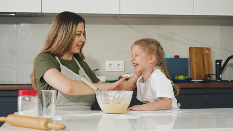 cheerful-mother-cleans-daughter-face-from-flour-at-table