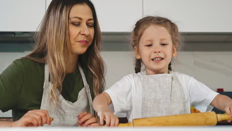mother-gives-little-girl-wooden-pin-to-roll-dough-at-table