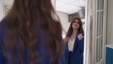 Woman-tries-on-elegant-blue-coat-looking-in-mirror-in-room