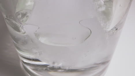 Pouring-water-into-glass-with-ice-cubes-on-white-table