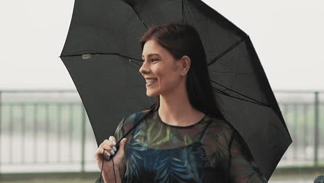 Smiling-woman-with-black-umbrella-stands-under-light-rain