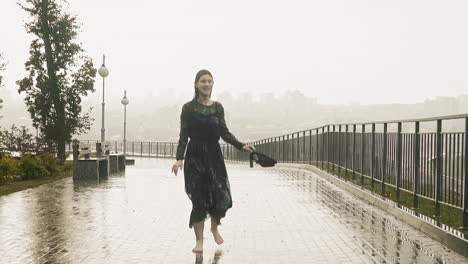 Barefoot-lady-runs-and-turns-with-shoes-along-street-at-rain