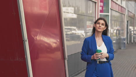 Woman-in-blue-suit-walks-holding-cup-of-coffee-along-street