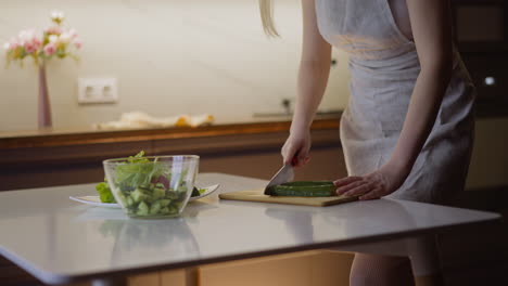 Young-wife-cuts-cucumber-cooking-tasty-salad-at-table