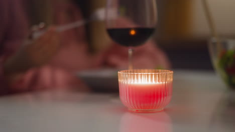 Candle-in-holder-burns-on-table-while-person-eats-dinner