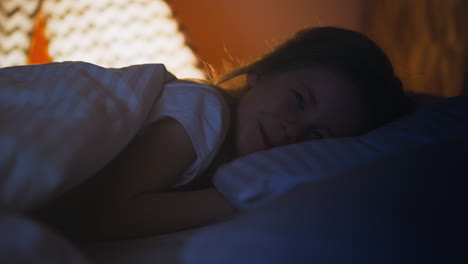 Little-girl-smiles-to-camera-under-soft-blanket-on-bed