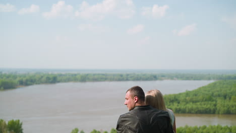 Man-embraces-beloved-woman-enjoying-view-of-tranquil-river