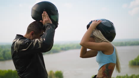 Man-and-woman-take-off-moto-helmets-against-large-lake