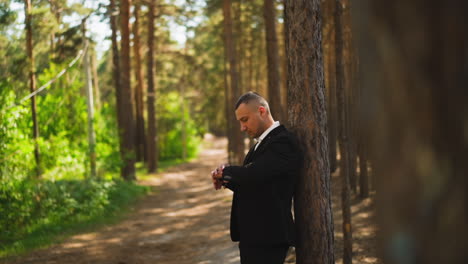 Man-in-suit-checks-time-waiting-for-girlfriend-in-forest