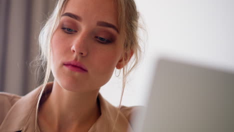 Focused-blonde-woman-looks-at-screen-of-modern-laptop