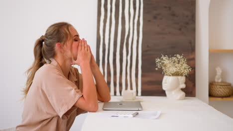Tired-freelance-woman-sits-near-closed-laptop-at-white-table