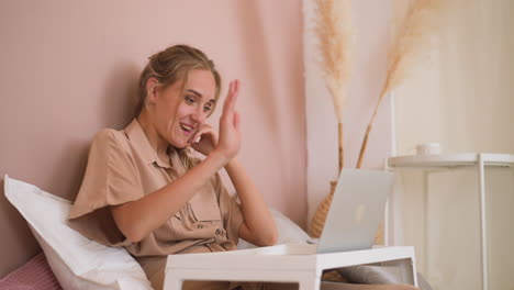 Blonde-woman-enjoys-talking-on-videocall-via-laptop-in-bed