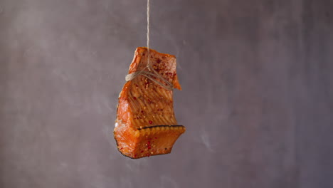 Piece-of-smoked-trout-with-spices-hangs-on-rope-at-steam