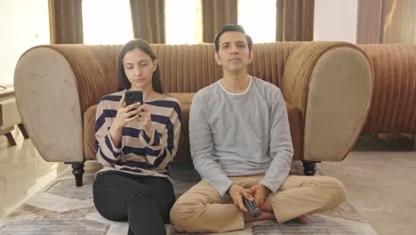 Indian-husband-watching-TV-and-wife-is-busy-on-phone