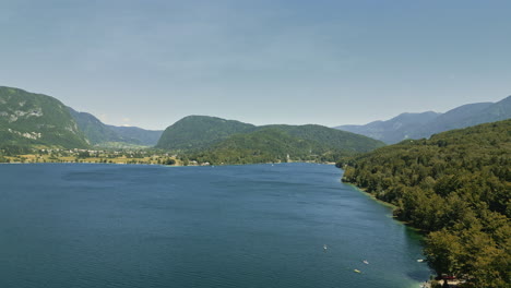 Drone-flies-along-calm-serene-waters-of-Lake-Bohinj-Slovenia,-mountains-surround