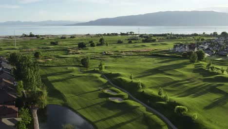 Drone-rises-above-golf-course-with-long-shadows-cast-by-sunset-glow,-vineyard-utah
